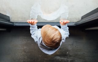 Pieni lapsi nojaa ikkunaan ja katsoo ulos ikkunasta