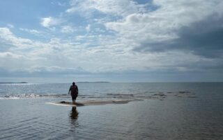 Tumma hahmo kävelee horisontissa autiolla rannalla.