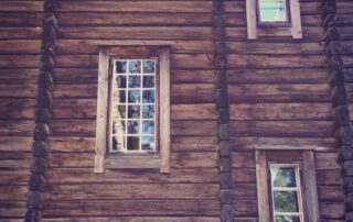 Tumma hirsiseinä, jonka pikkuruutuisista ikkunoista heijastuu luontoa