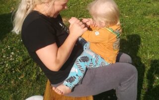 Pellavapäinen äiti leikityttää taaperoikäistä lasta sylissään.